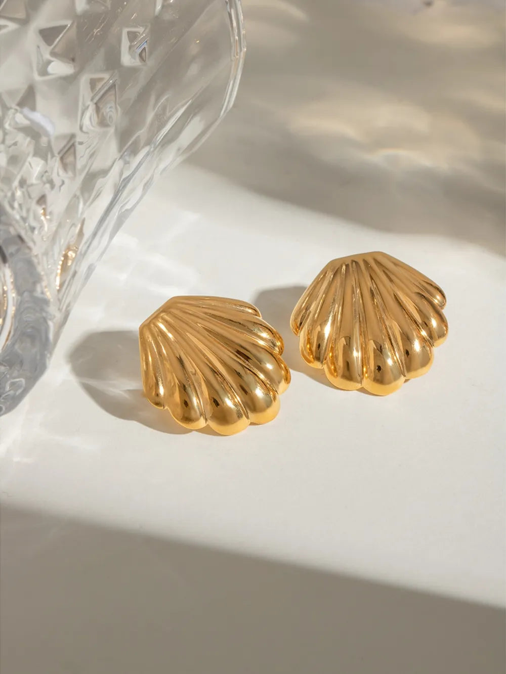 Gilded scallop ear studs in gold, featuring a textured shell design.