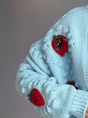 Pastel blue knit cardigan with embroidered strawberry details on the sleeve.