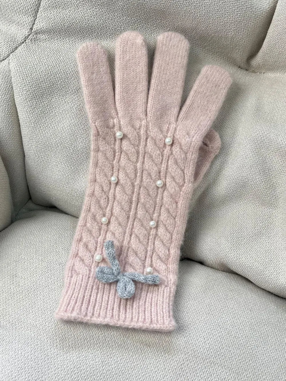 Blush pink cable knit gloves with pearl embellishments and a grey bow detail.