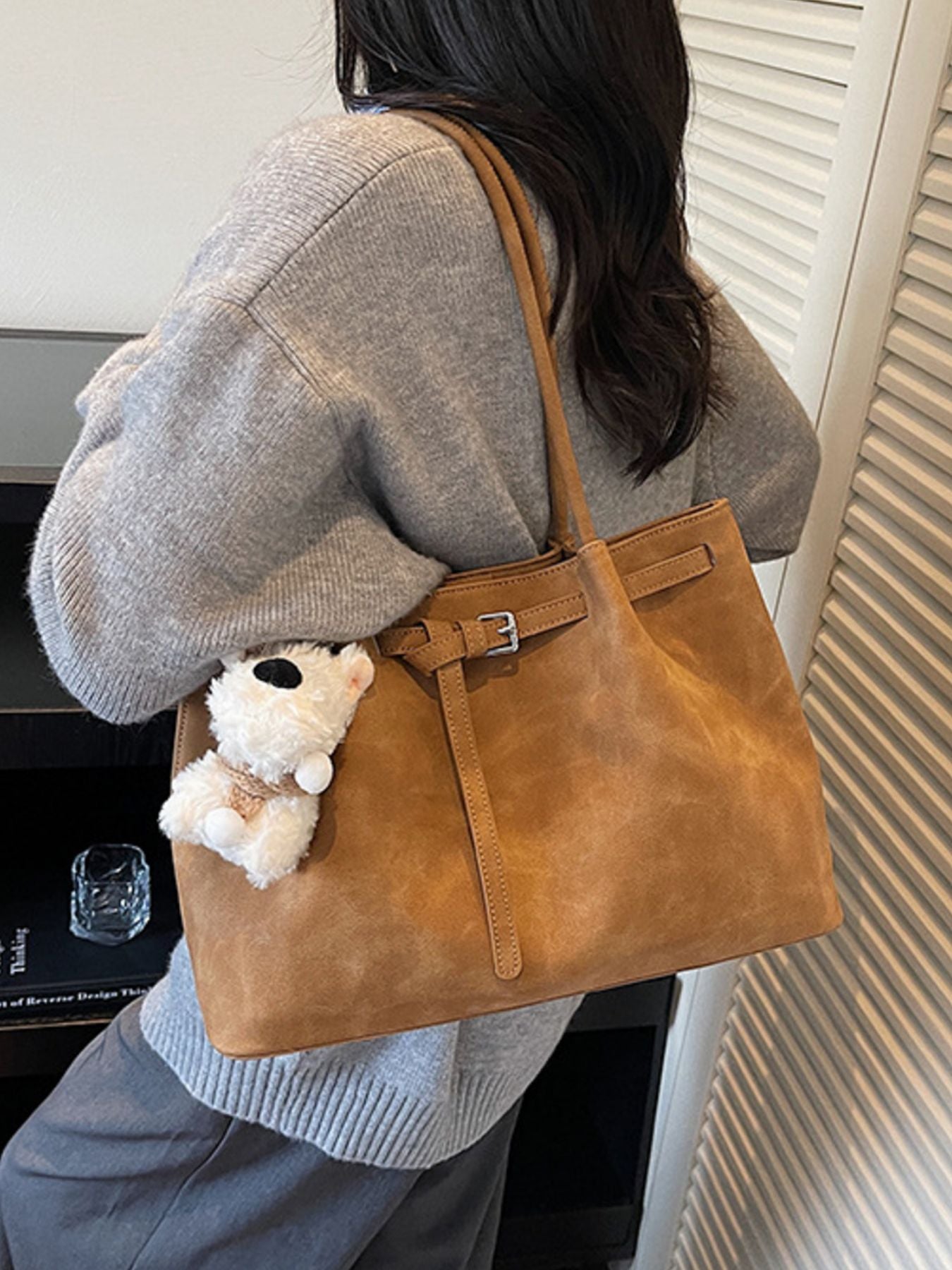 Brown suede shoulder bag with buckle accent and decorative strap, featuring a plush charm.