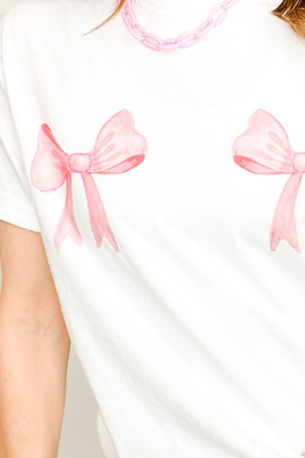White t-shirt with double pink watercolor bow graphic and pink chain necklace.
