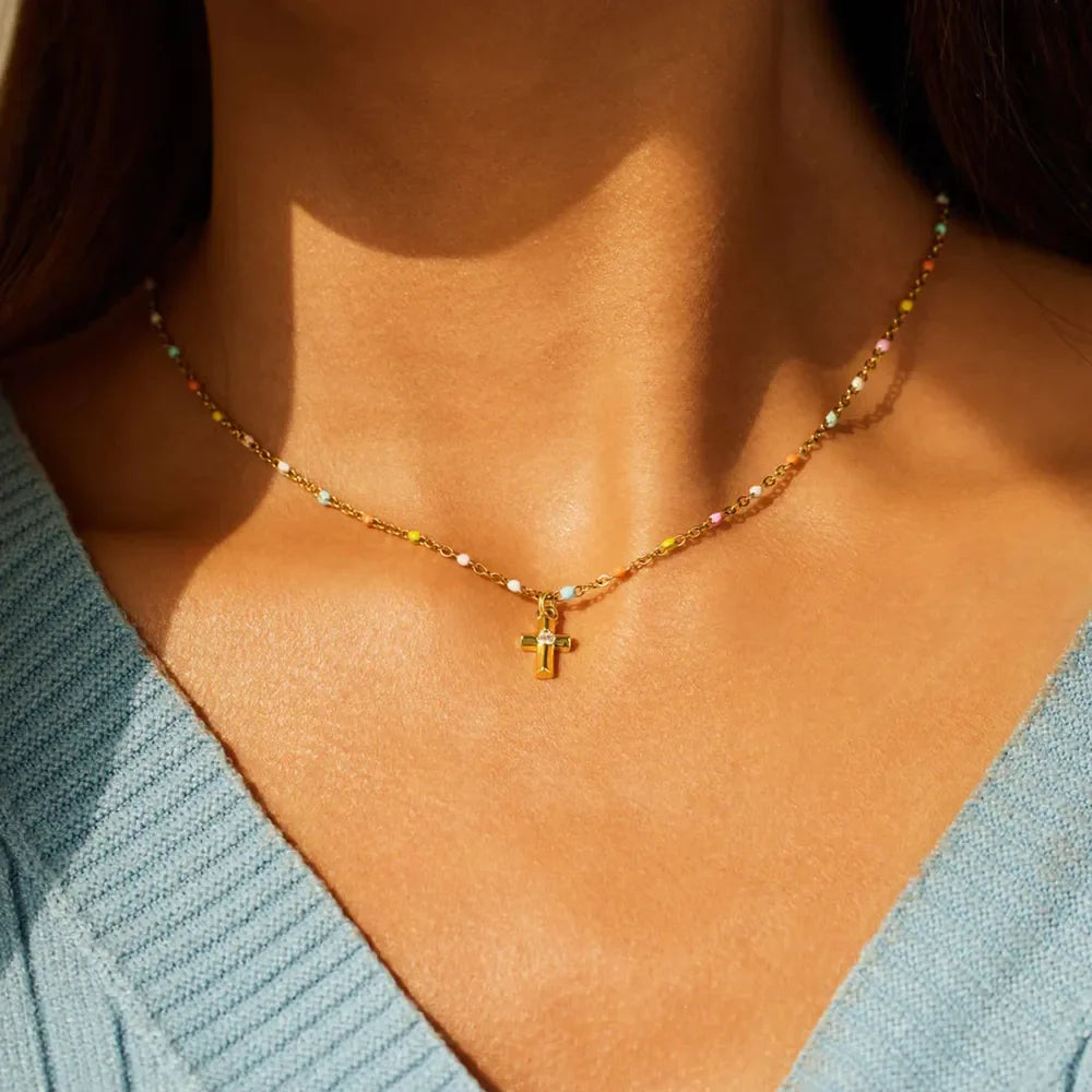 Gold necklace with rainbow beads and a small cross pendant.