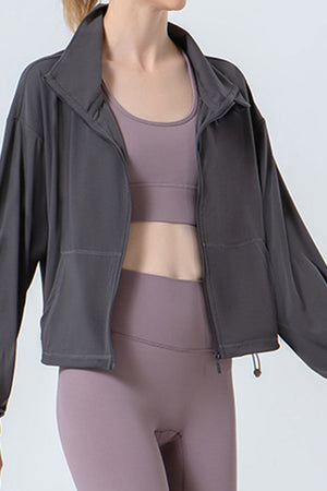 Dark gray active jacket with gathered hemline and zip front, featuring pockets.