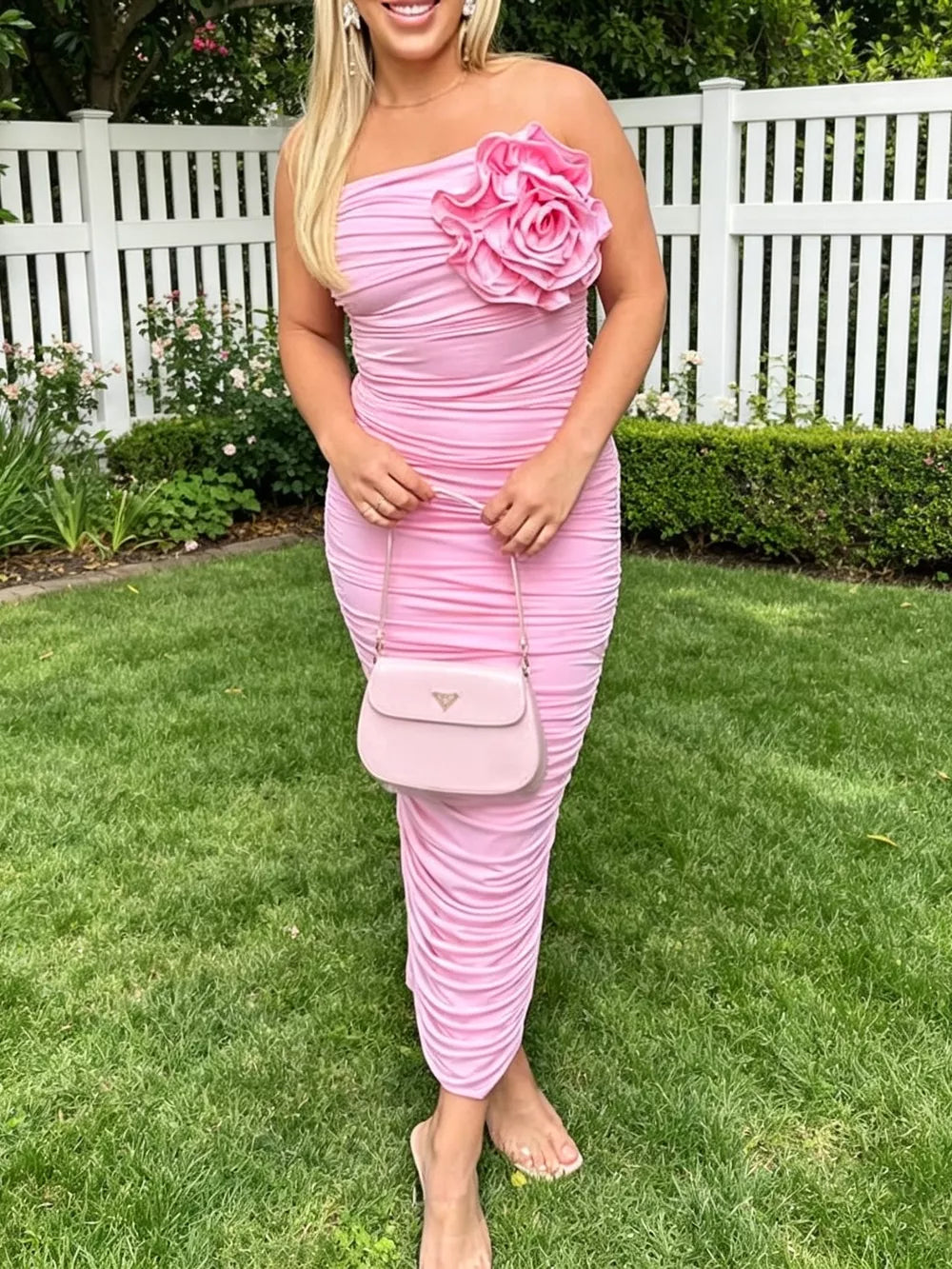 Pink ruched bodycon midi dress with floral appliqué and one-shoulder neckline.