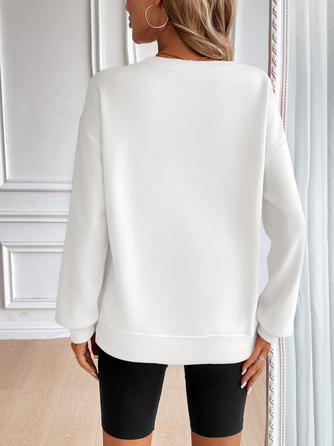 White relaxed fit sweatshirt with crewneck and long sleeves, styled with black biker shorts.