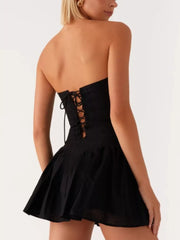 Black ruffled tube dress with lace-up back detail and flared skirt.