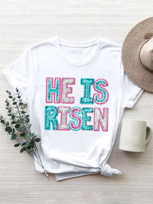 White crewneck t-shirt with sequin-textured "He Is Risen" graphic in aqua, pink, and silver.