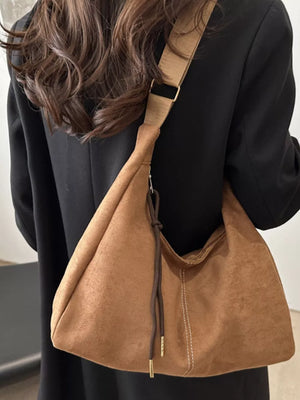 Brown suede crossbody bag with adjustable strap and drawstring detail.