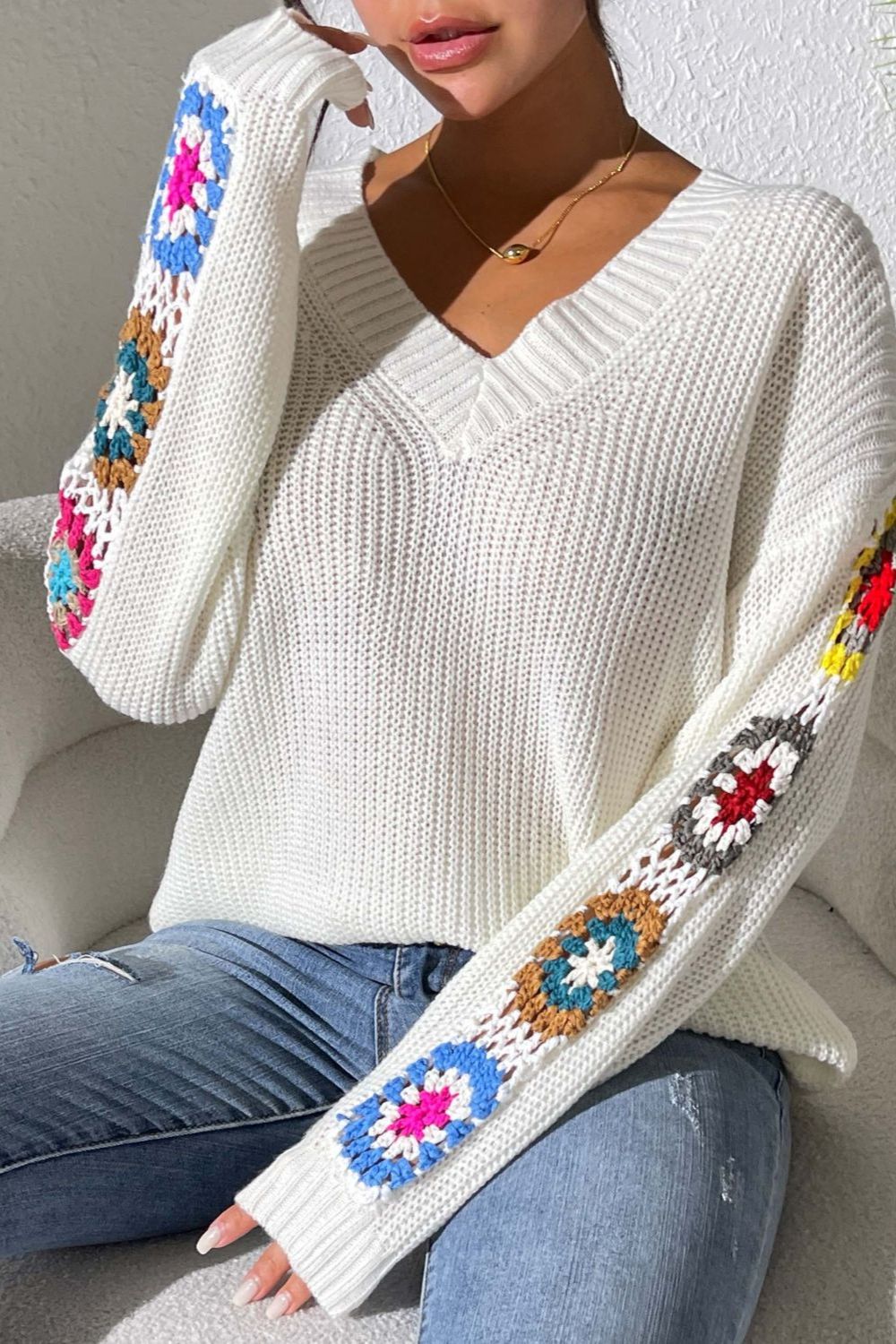 White knit sweater with colorful granny square sleeve details and V-neck.