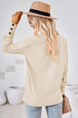 Cream textured v-neck blouse with button cuff detail.