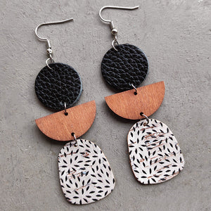 Geometric layered leather and wood earrings with black, wood, and patterned cork.