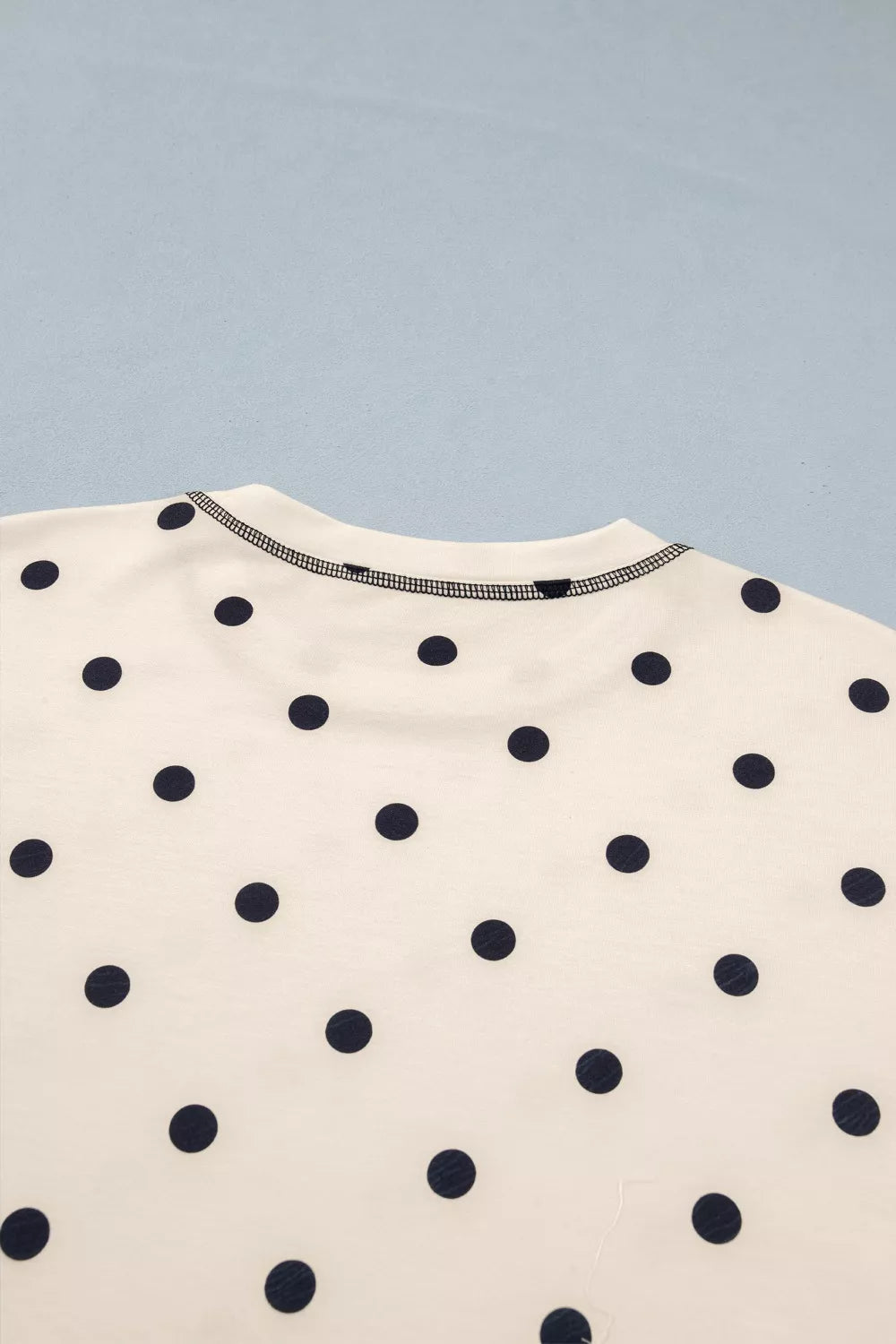 Cream polyester bikini top with navy polka dots and contrast stitching.