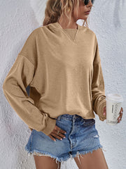 Tan boxy hooded sweatshirt with V-neck detail and split hem, styled with denim shorts.