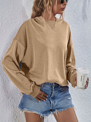 Tan boxy hooded sweatshirt with V-neck detail and split hem, styled with denim shorts.
