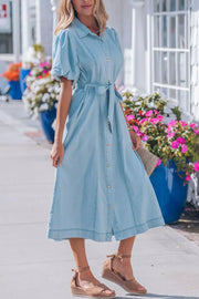Light blue denim midi dress with puff sleeves, collar, button front, and belted waist.