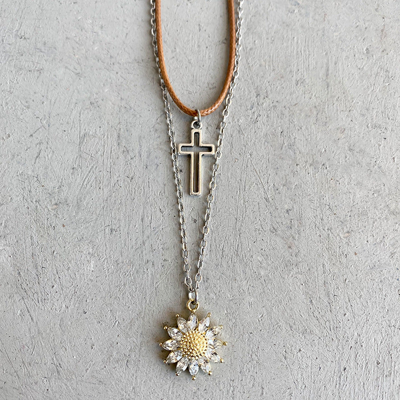 Layered necklace set with silver cross and crystal sunflower charm on brown cord and silver chain.