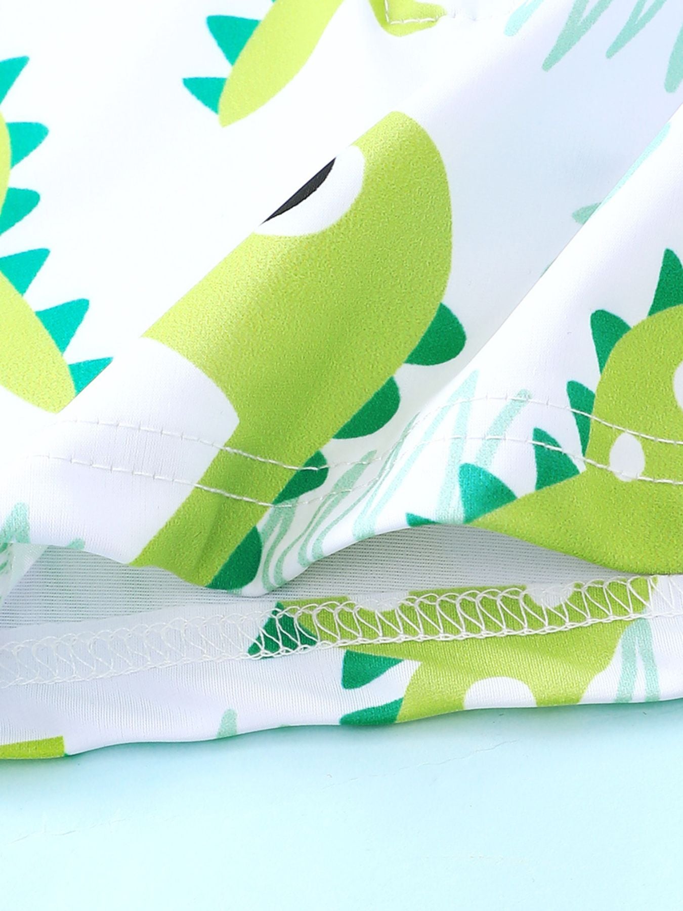 Children's swimwear set with a green dinosaur print on white fabric.
