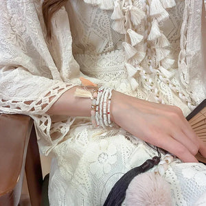 White beaded tassel stacked bracelet set with pink stones and red accents.