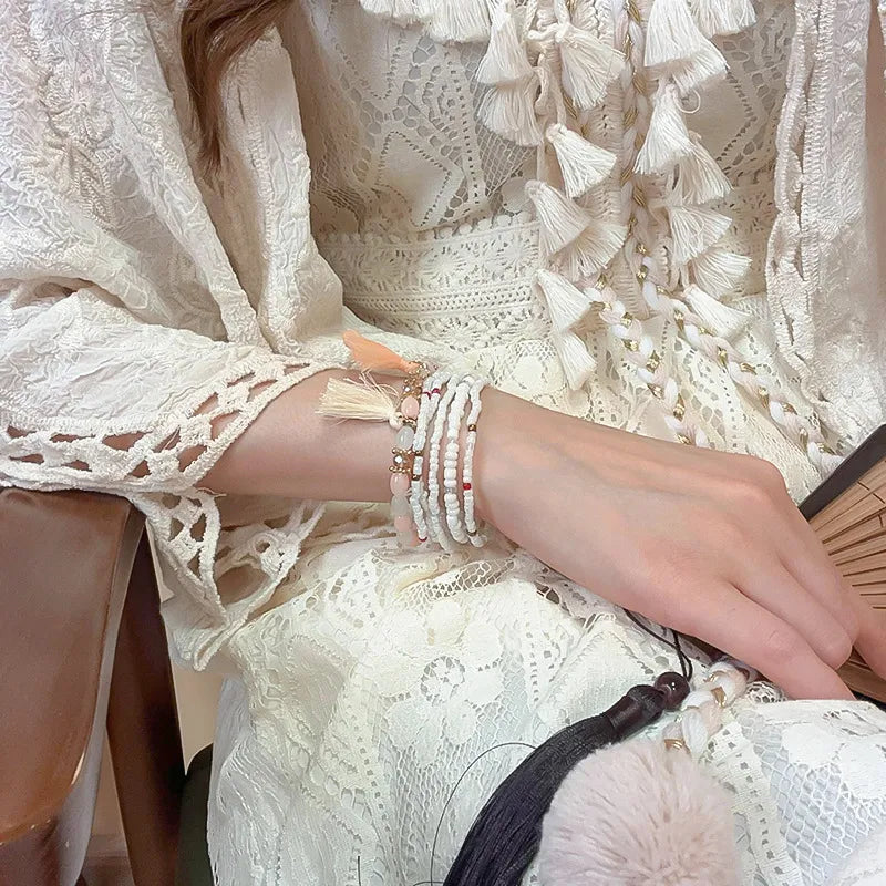 White beaded tassel stacked bracelet set with pink stones and red accents.