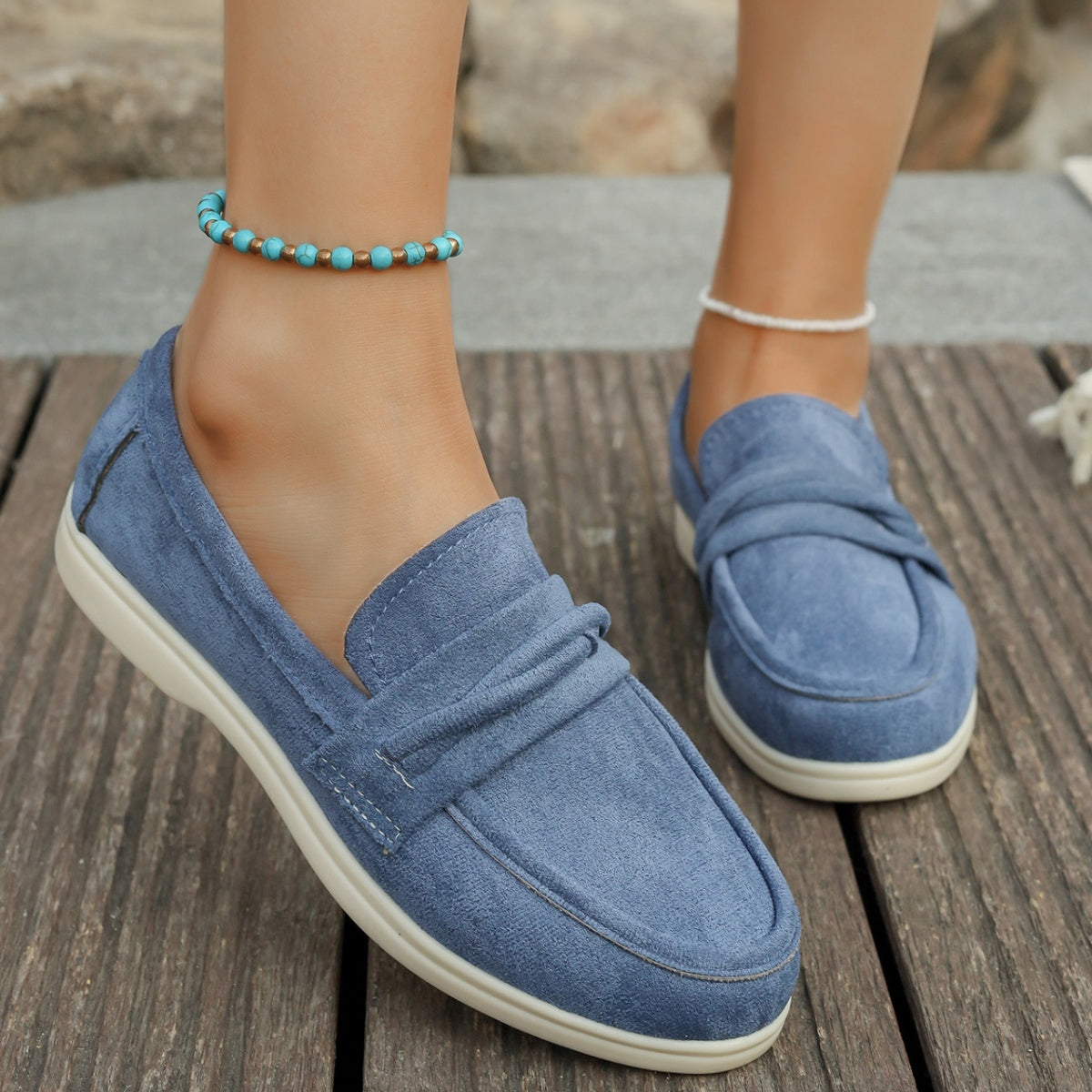 Blue slip-on loafers with ruched detail and white soles.