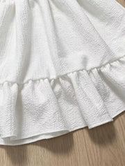 White baby dress with textured fabric and ruffle hem detail.