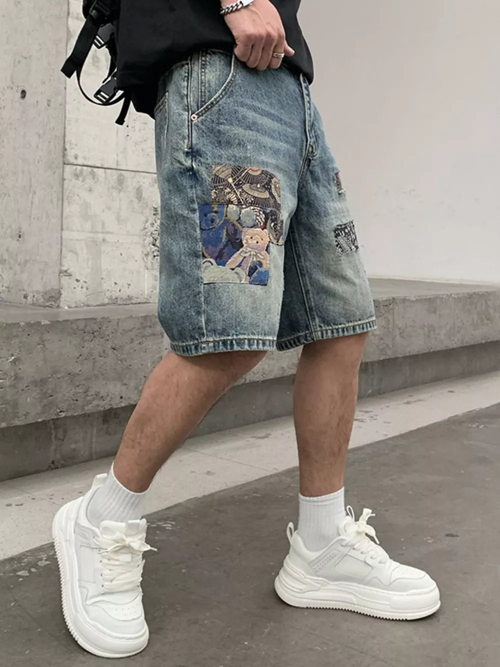 Men's denim shorts in light wash with graphic patchwork details and teddy bear motifs.