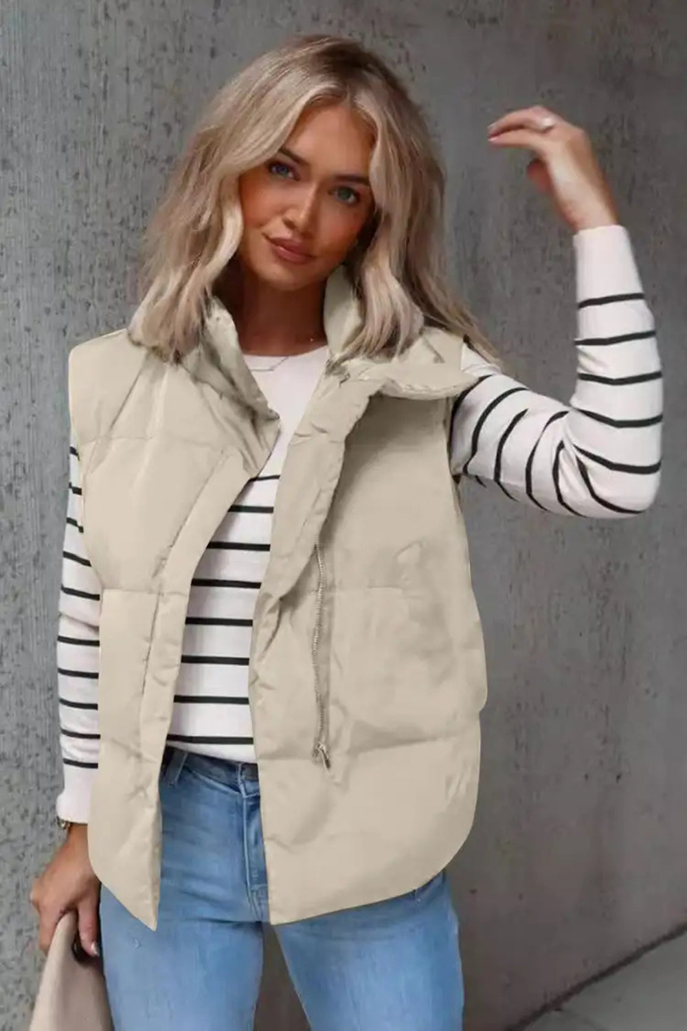 Padded stand collar vest in beige with a zip front, styled over a striped long-sleeve shirt.