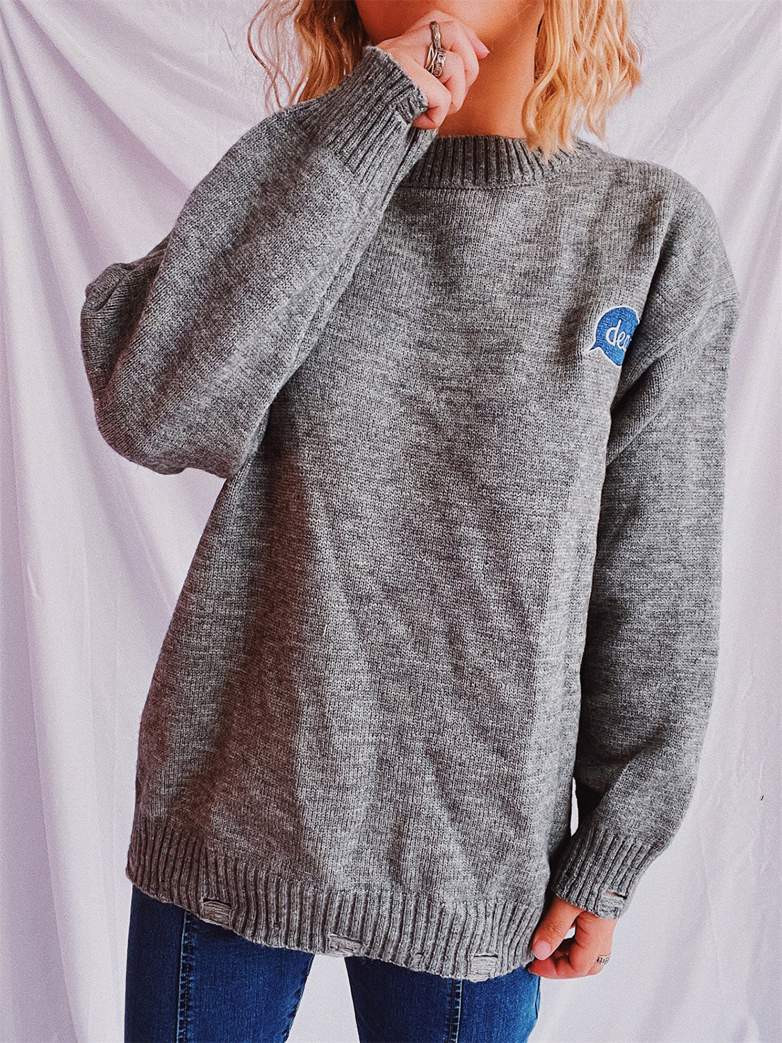 Dark gray relaxed knit sweater with embroidered blue speech bubble detail on chest.