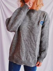 Dark gray relaxed knit sweater with embroidered blue speech bubble detail on chest.