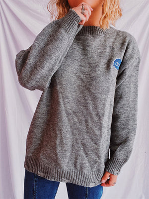 Dark gray relaxed knit sweater with embroidered blue speech bubble detail on chest.