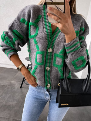 Geometric chain knit cardigan in grey with green accents, button front, V-neck, and long sleeves.