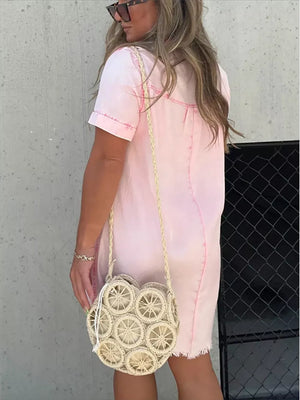 Pink short sleeve above knee dress with contrast stitching and frayed hem, worn with a straw crossbody bag.