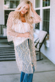 Beige sequin duster with flared sleeves and fringe detail, worn over a white tank and jeans.