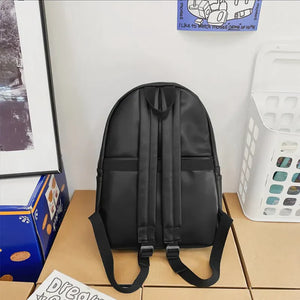 Black minimalist leather backpack with adjustable straps and a front pocket detail.