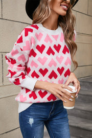 Pink and red heart knit sweater with crewneck and white cuffs.