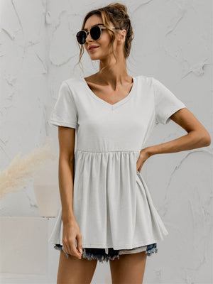 White V-neck tee with gathered waistline and short sleeves, styled with denim shorts.