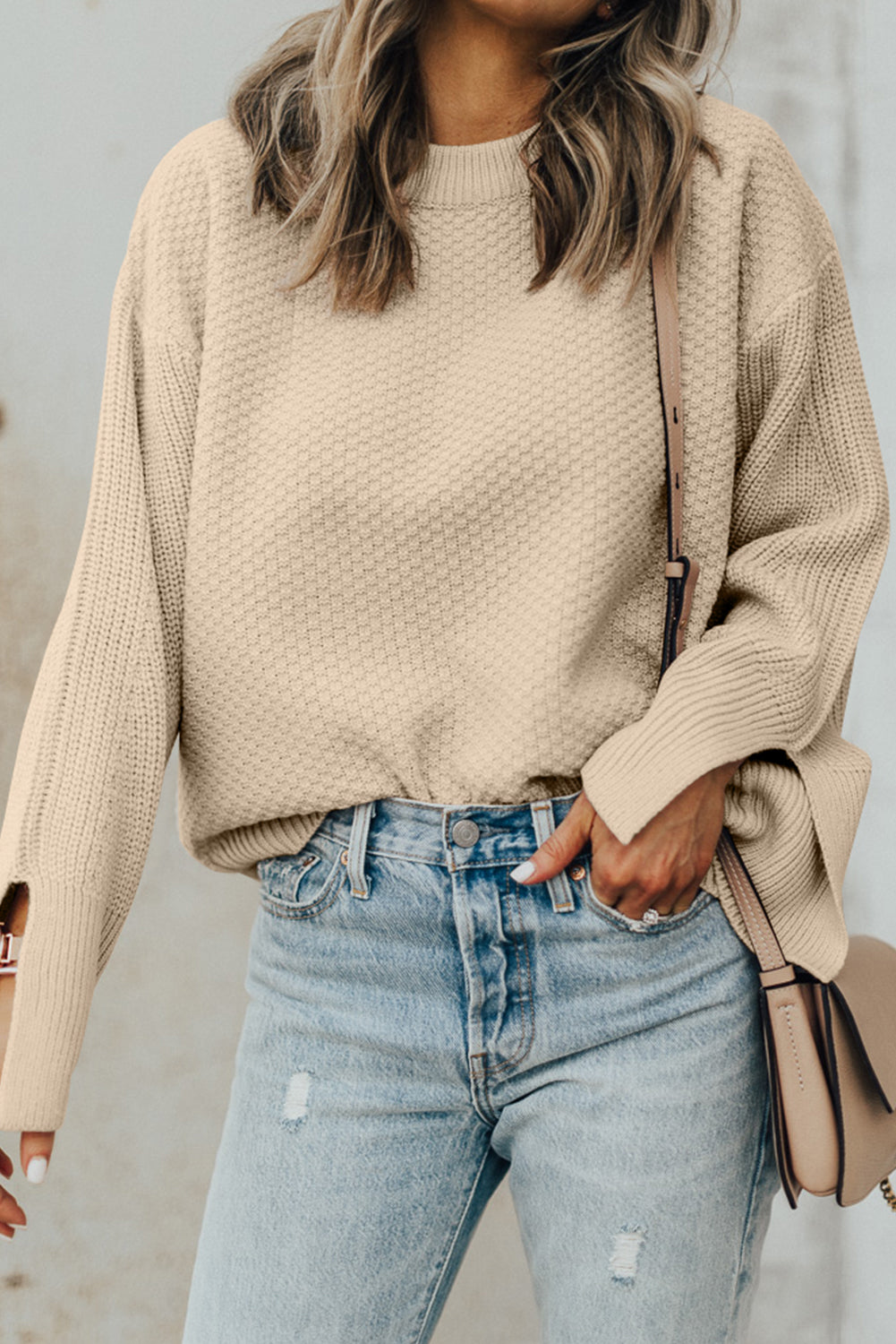 Beige textured knit sweater with crew neck and slit sleeves, styled with jeans.