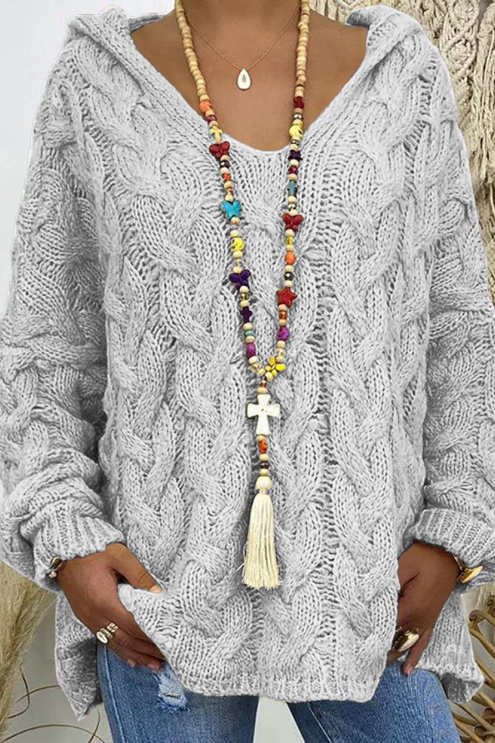 Light gray cable knit hooded cocoon sweater with V-neck and tassel detail.