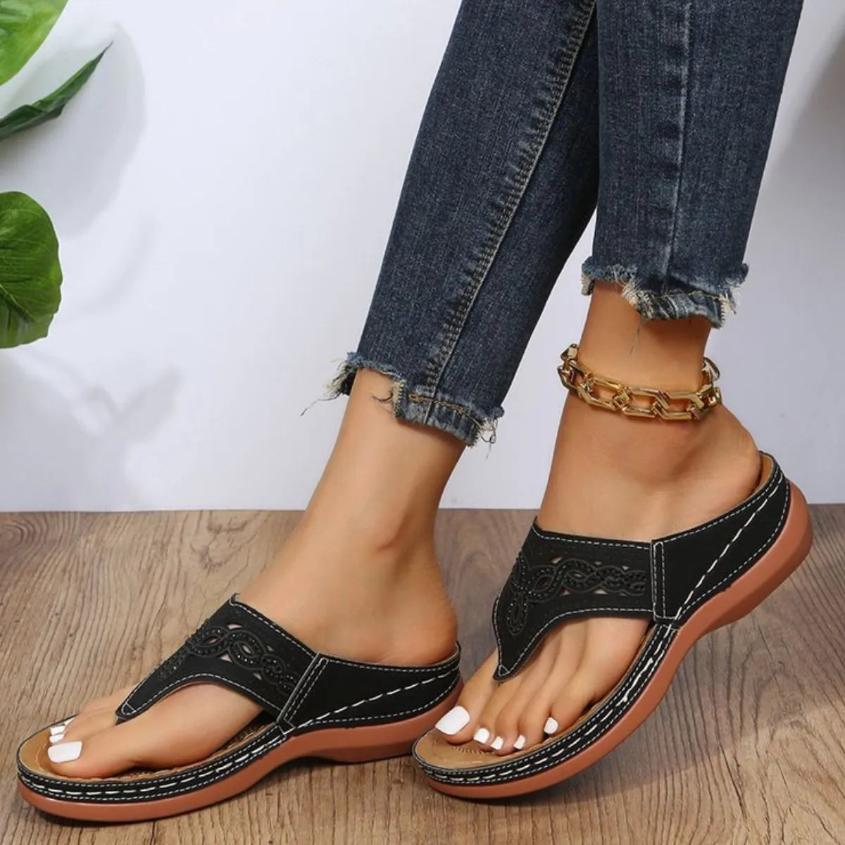 Black laser-cut thong sandals with white stitching and architectural detail.