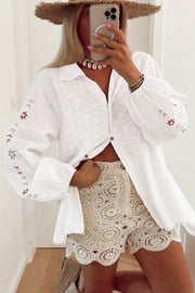 White embroidered eyelet blouse with poet sleeves and button front, styled with crochet shorts.