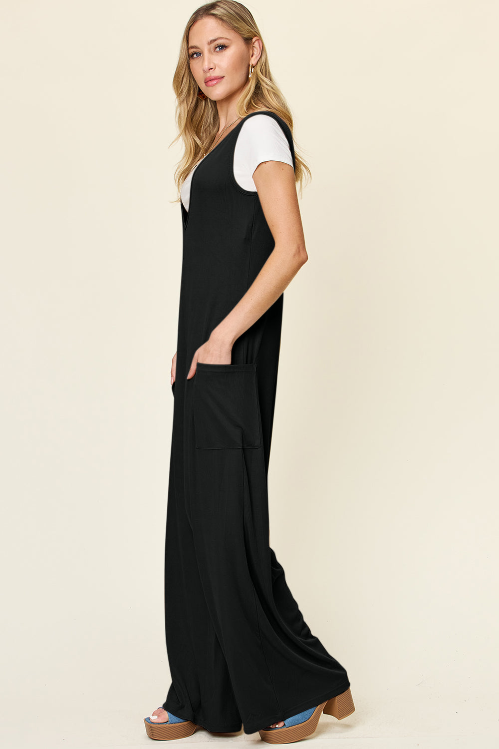 Black wide-leg pocket jumpsuit with deep V-neck, shown layered over a white t-shirt.
