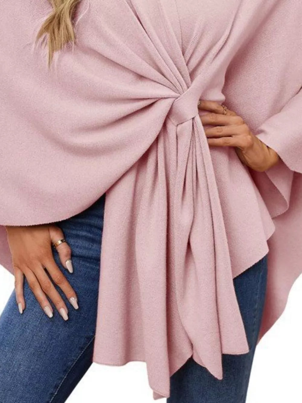 Pink knit cape top with a tie-front detail and draped elegance, styled with jeans.