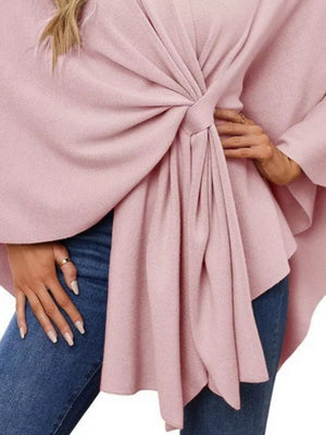 Pink knit cape top with a tie-front detail and draped elegance, styled with jeans.