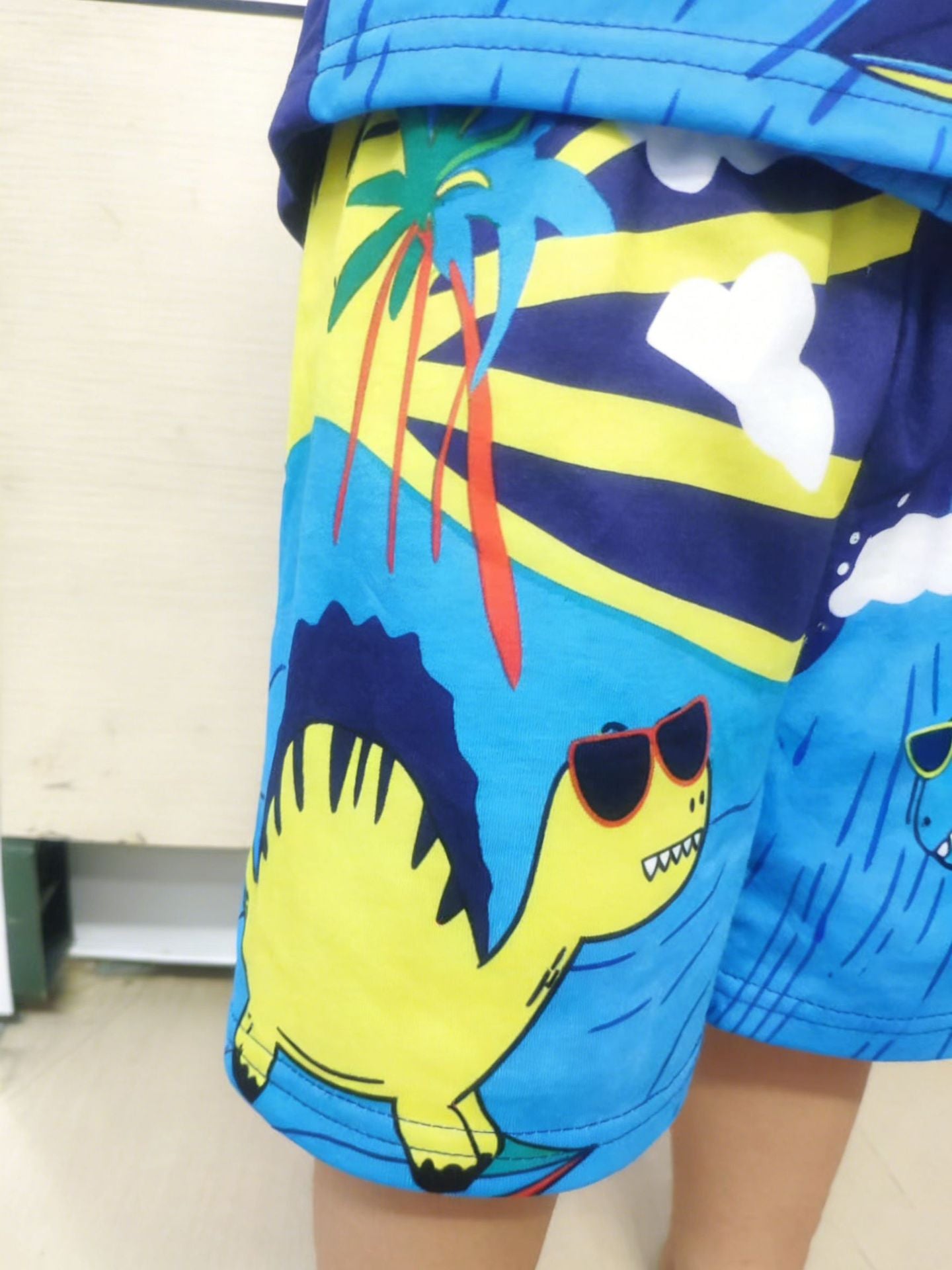 Toddler shorts with blue, yellow, and navy dinosaur graphic print and palm trees.