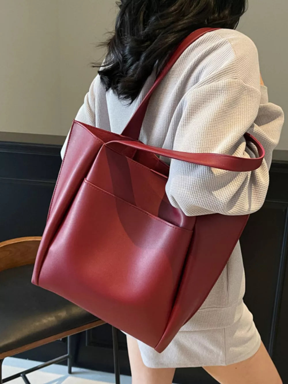 Wine red pu leather tote bag with exterior pocket, worn by a woman.