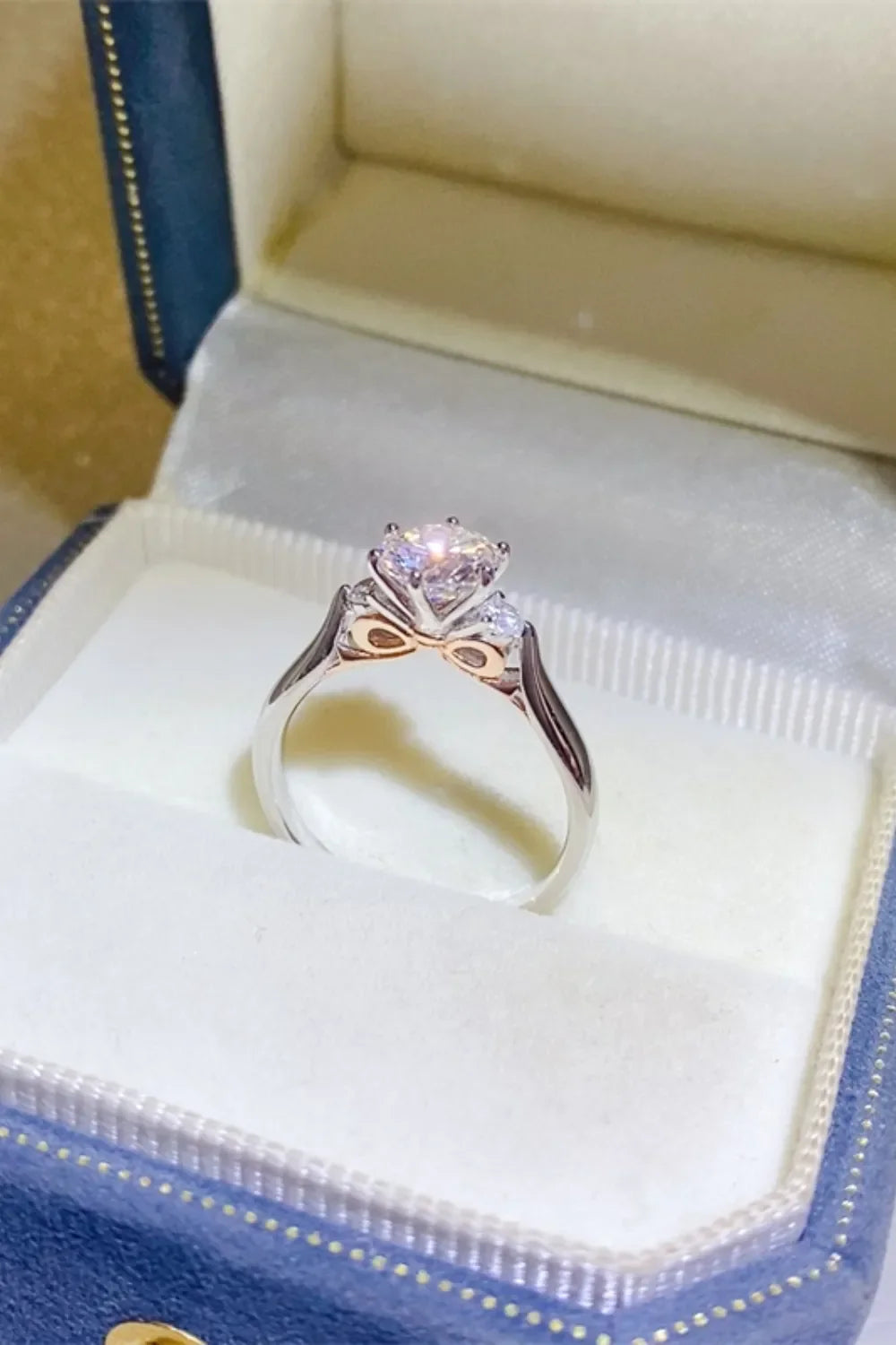 Silver moissanite trilogy ring with rose gold accents and a bow detail.