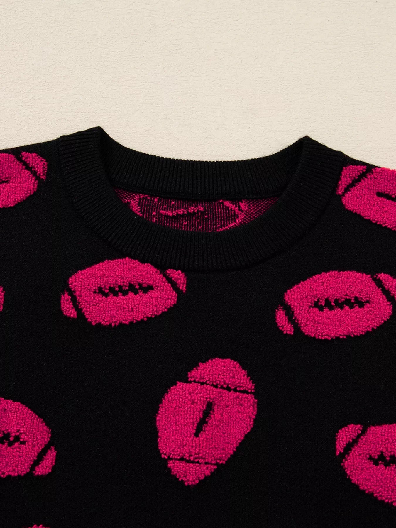 Black knit sweater with a playful pink football pattern and crew neck.