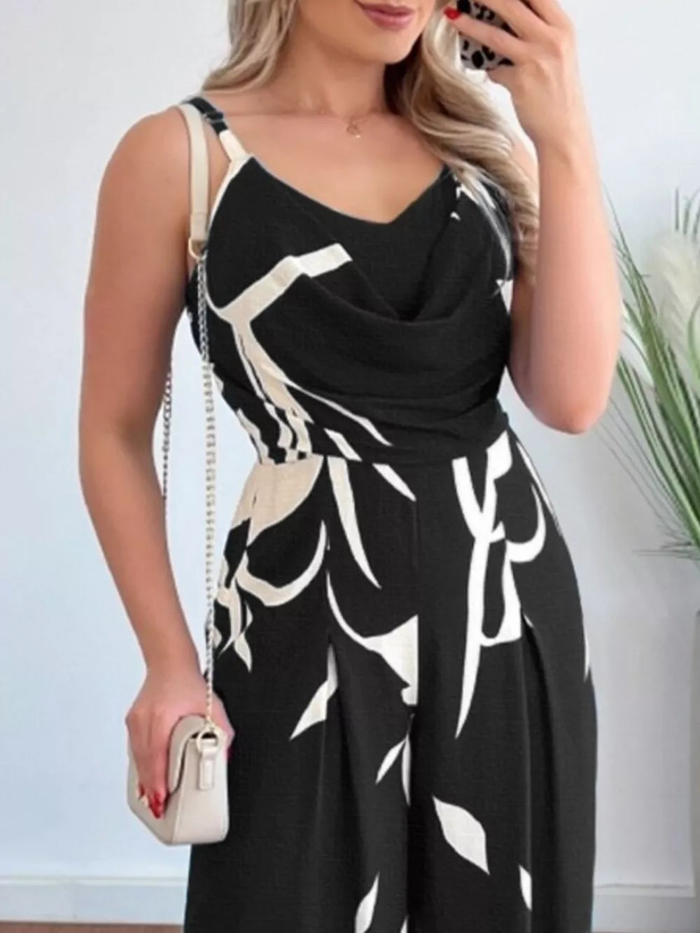 Black abstract leaf print wide-leg jumpsuit with cowl neck and adjustable straps.