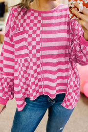Hot Pink knit top with asymmetrical checkered and striped patchwork, crew neck, long sleeves, and pocket detail.