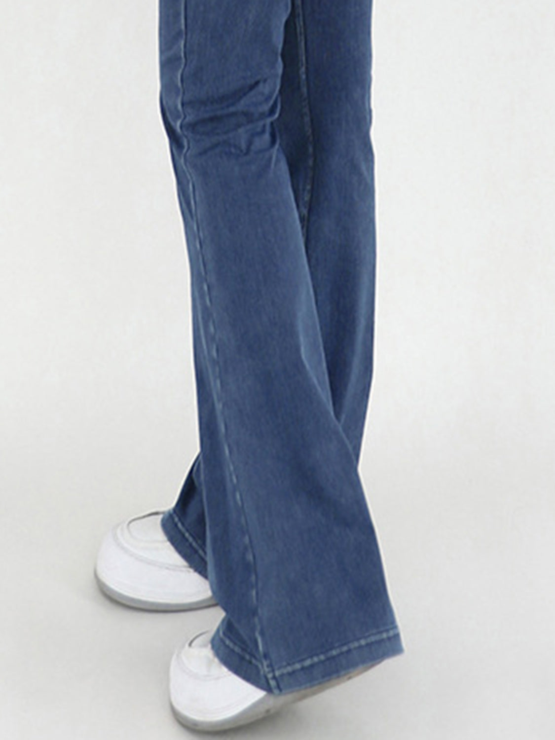 Medium wash denim flare jeans with a crossover waist detail, styled with white sneakers.
